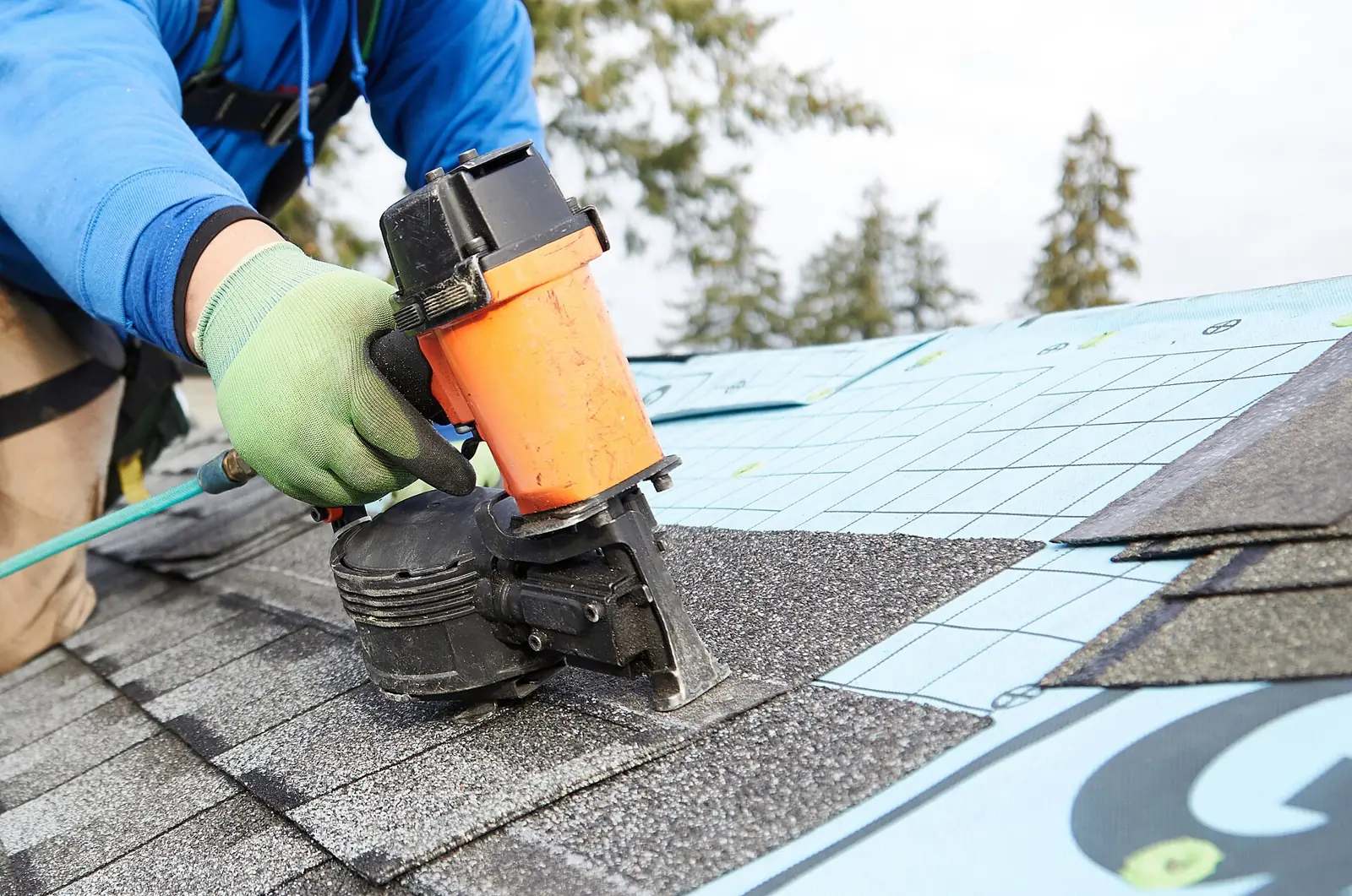 Hands using a nail gun to secure roof shingles.