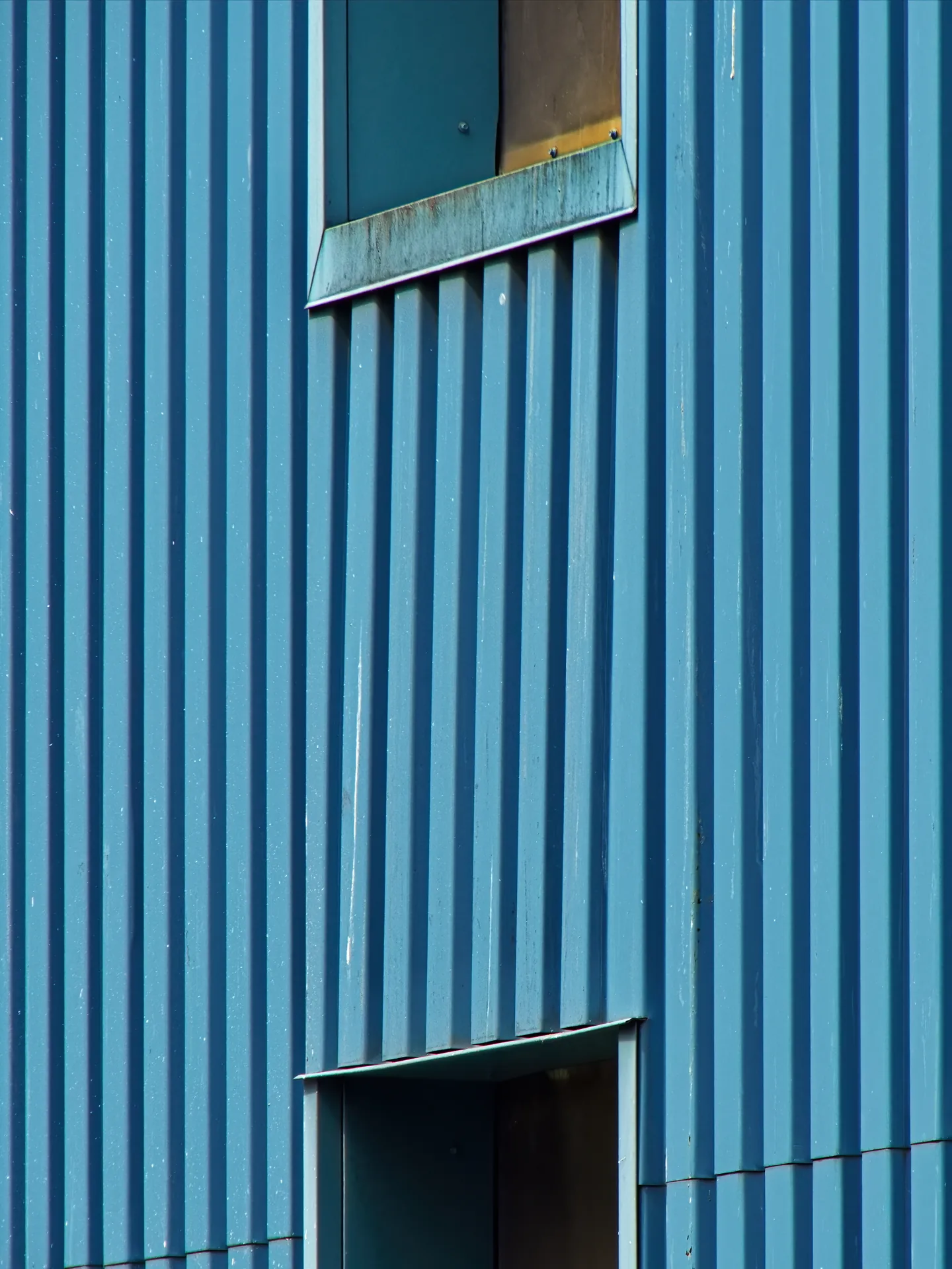 Blue profiled industrial cladding with recessed openings.