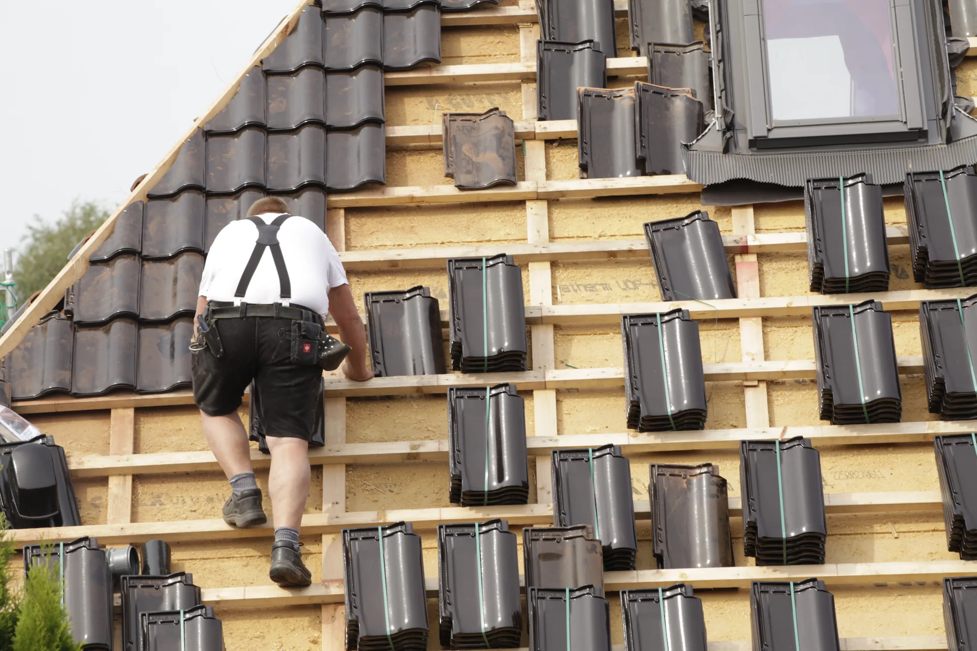A roofer installing dark tiles around an exposed roof structure and rooflight.